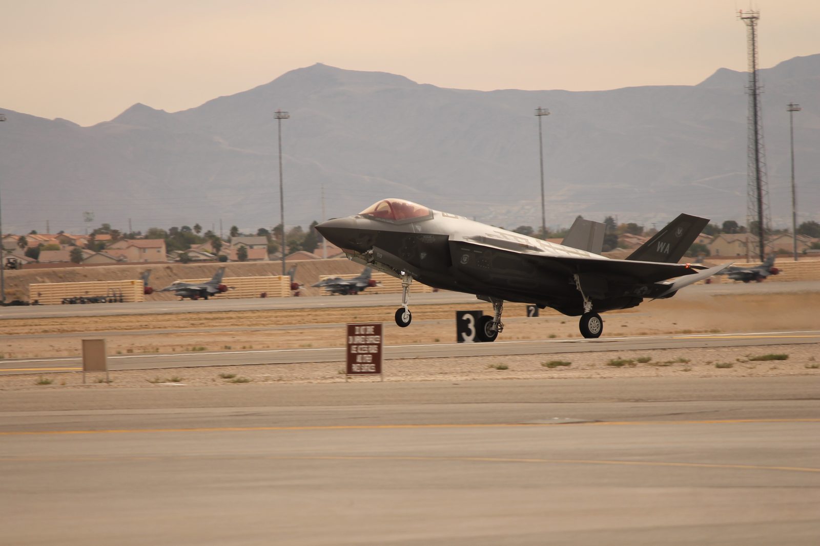 An F-35A Lightning II landing, full profile with landing gear extended, other jets visible in the background.