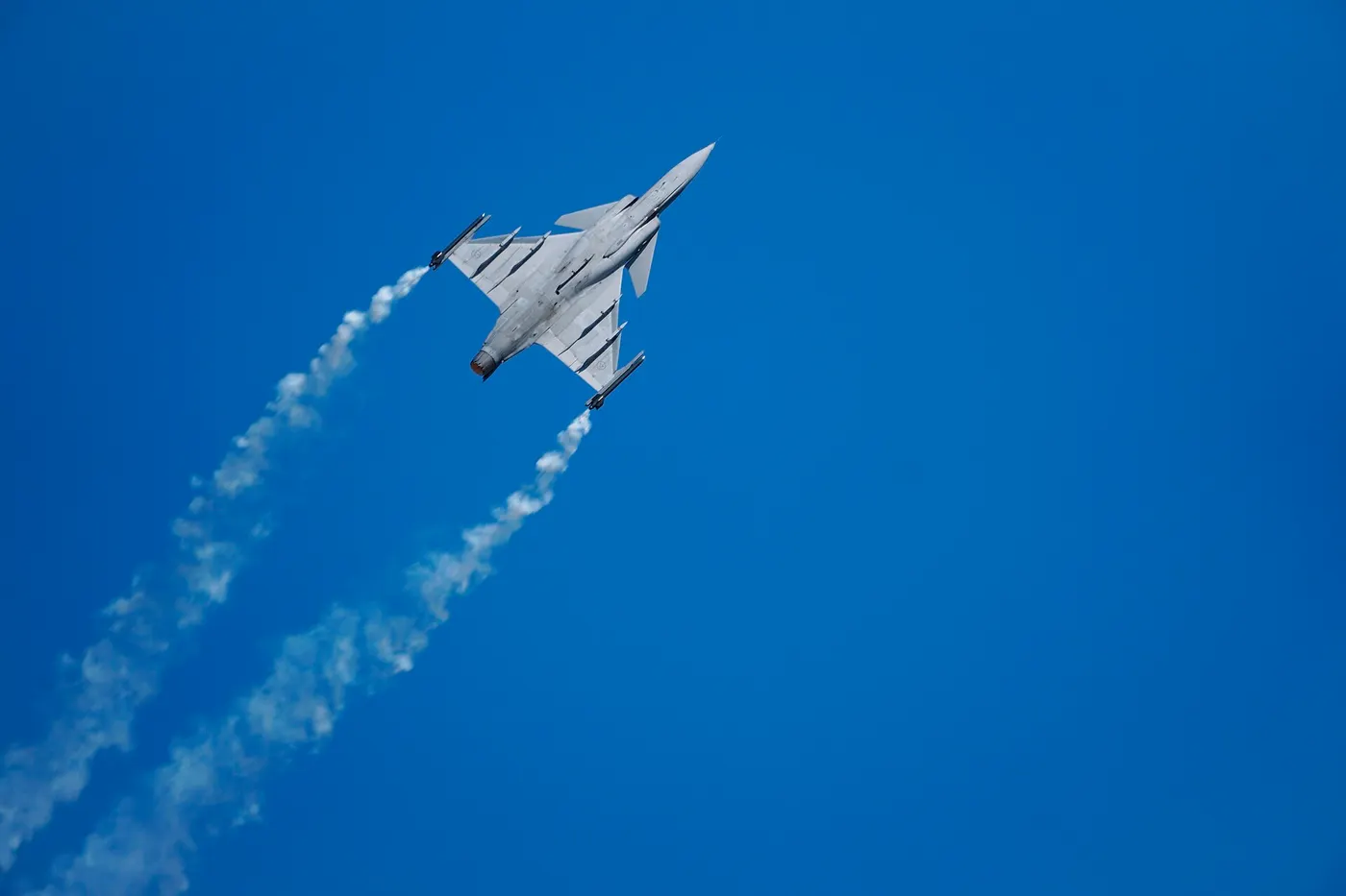 A JAS 39E Gripen fighter climbing steeply with visible smoke trails from its flares.