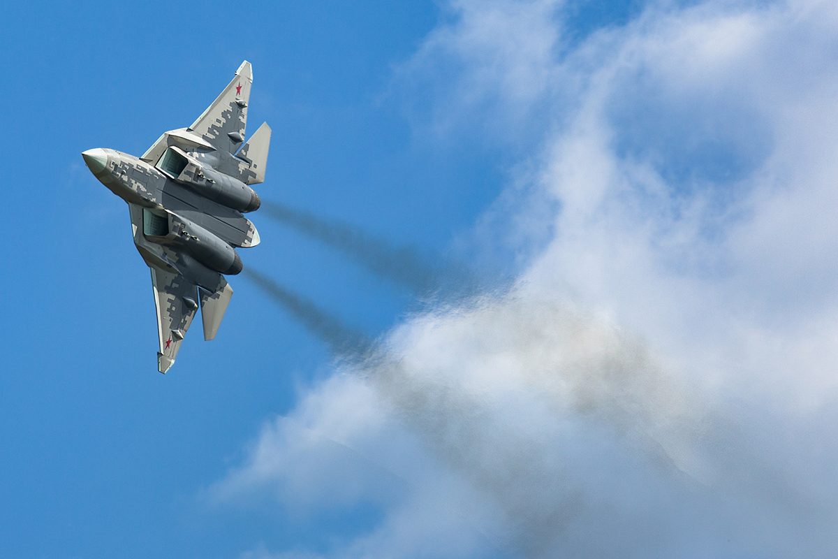 A Su-57 fighter jet banking, full underside profile with visible digital camouflage pattern.