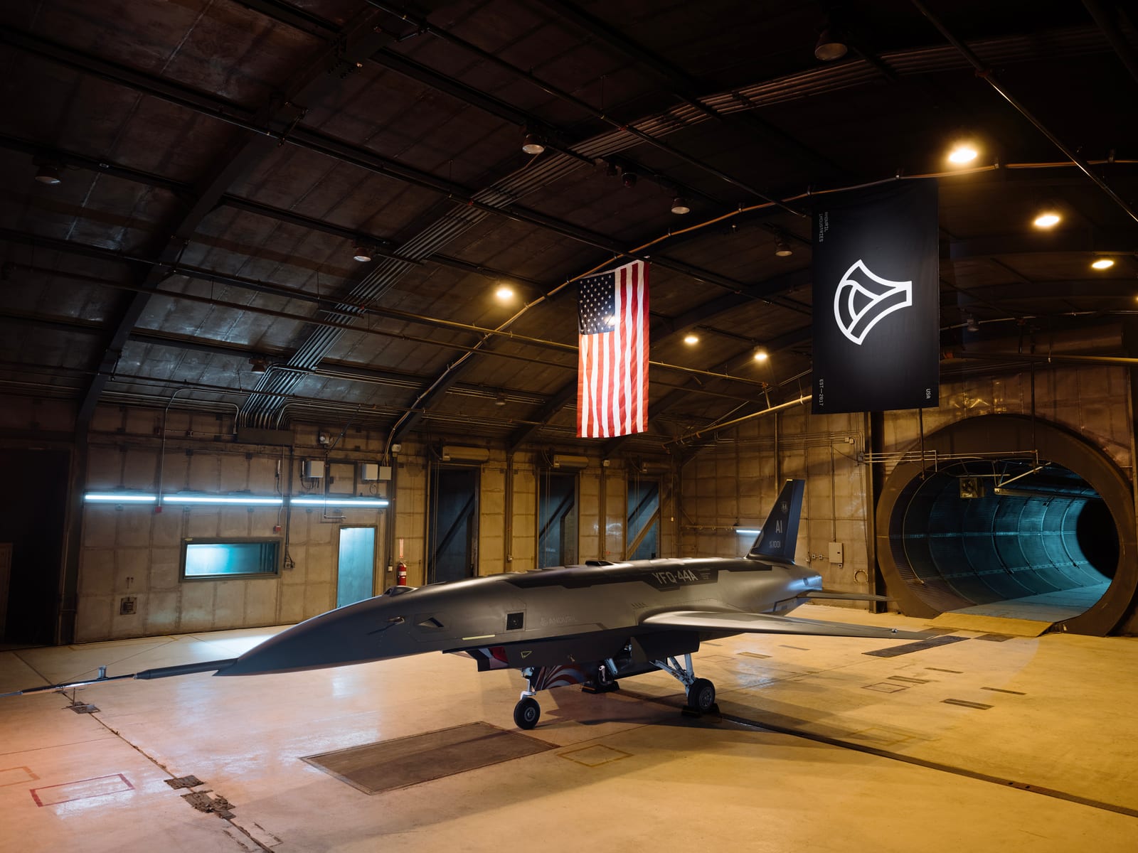 A YFQ-44A production representative test vehicle, a sleek gray jet-powered drone with a single vertical tail, staged inside an indoor testing chamber at an Anduril facility in Costa Mesa, California