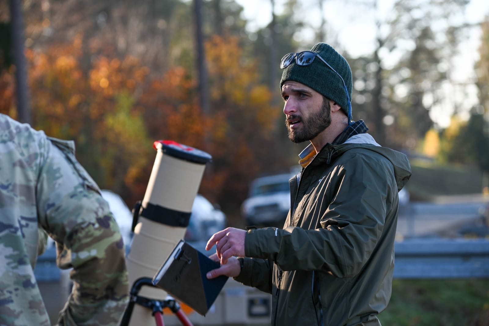 A U.S. Army contractor instructor stands beside soldiers examining a disassembled Switchblade 600 loitering munition system laid out on a table during a training session in a grassy field