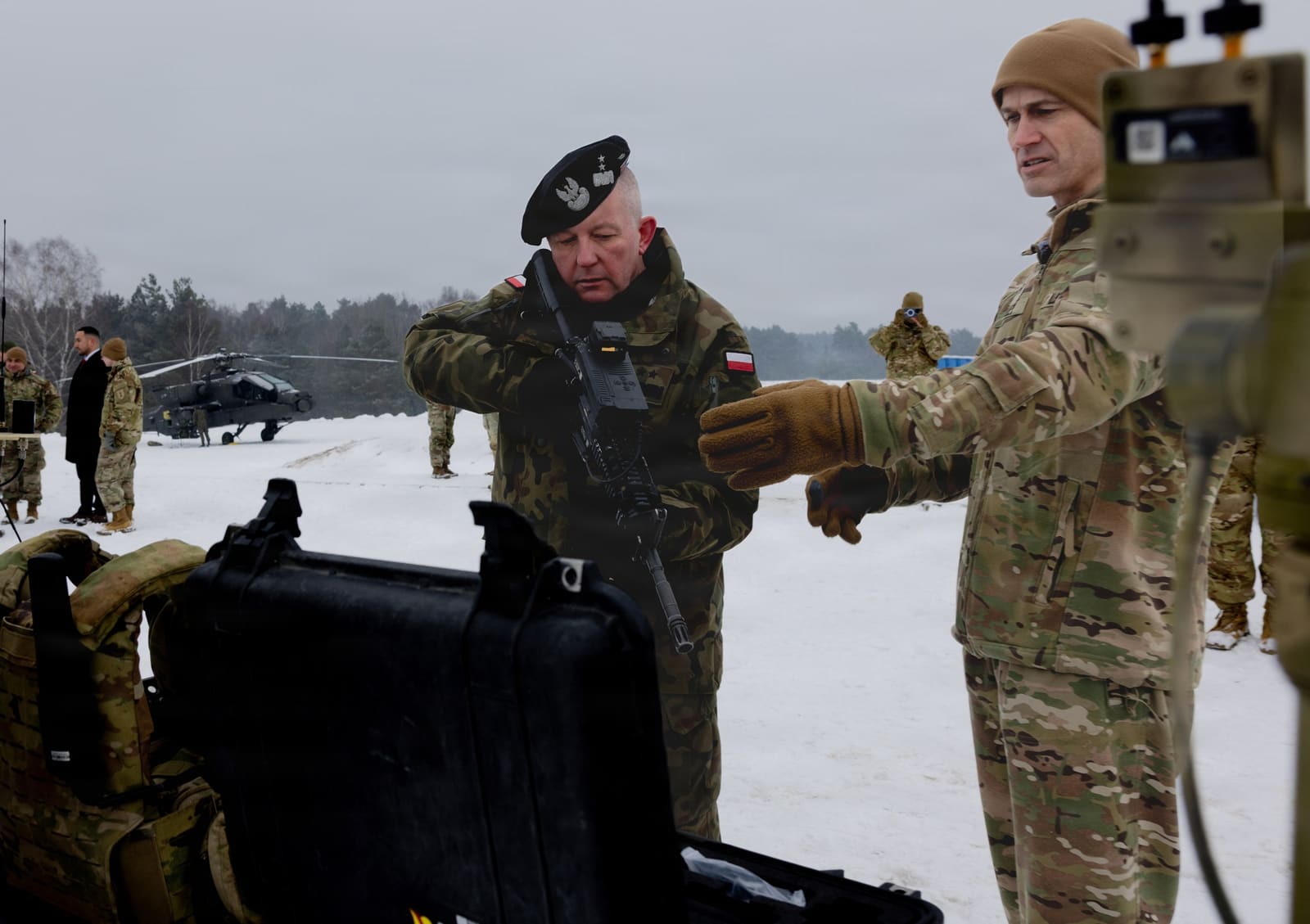 A Polish Land Forces general and a U.S. Army officer examine a rifle-mounted counter-drone optic during a snowy field exercise in Poland