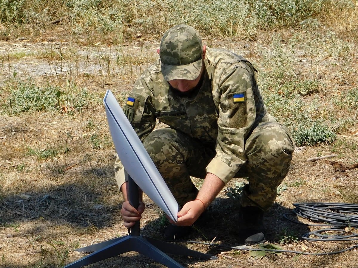A Ukrainian soldier installing a Starlink satellite internet terminal on its tripod mount in a field