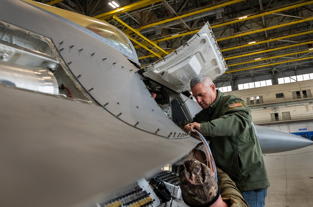 An aviation engineer works on modifying an F-16 Fighting Falcon's wiring as part of the VENOM Autonomy Kit installation at Eglin Air Force Base