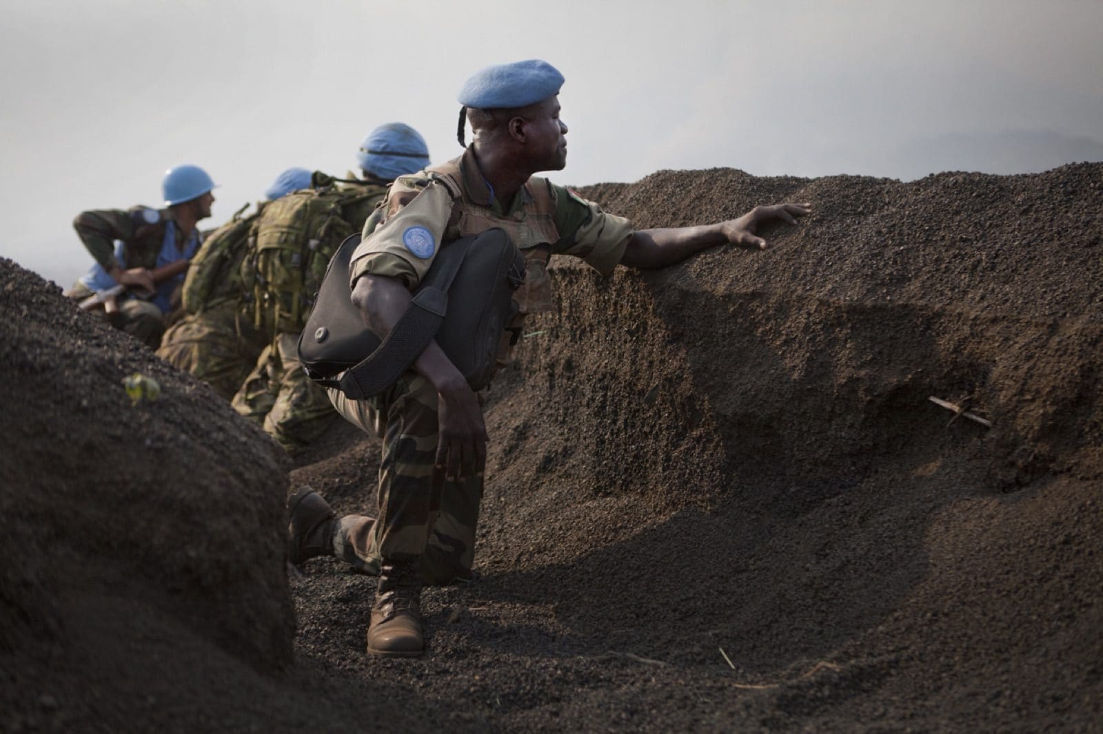 UN military observers take cover behind an earthen embankment on a hilltop overlooking a valley near Goma