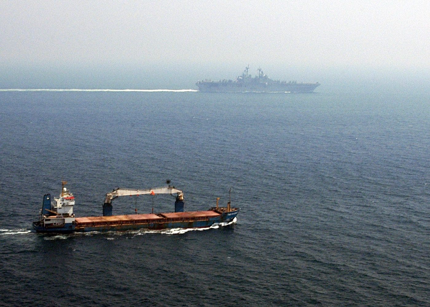 A merchant ship transits the Strait of Hormuz alongside a US Navy amphibious assault ship, illustrating the commercial shipping lane where three tankers were attacked on July 6, 2026