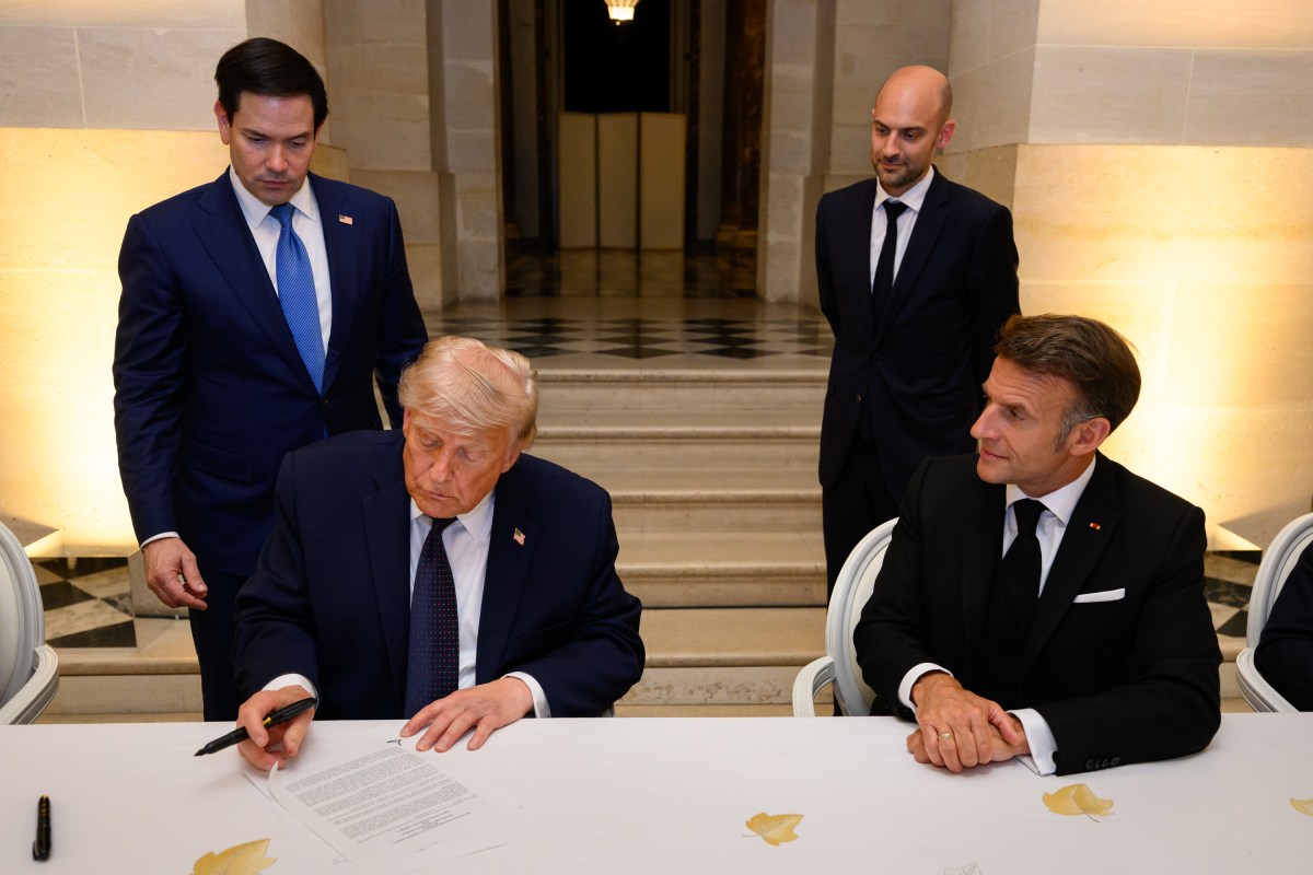 President Trump signs the Iran memorandum of understanding at a dinner table at the Palace of Versailles as other officials look on
