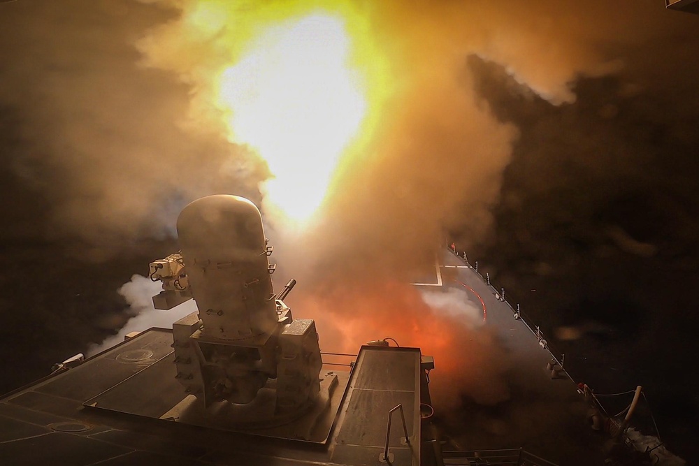The Arleigh Burke-class guided-missile destroyer USS Carney firing an interceptor at night while engaging Houthi missiles and drones in the Red Sea