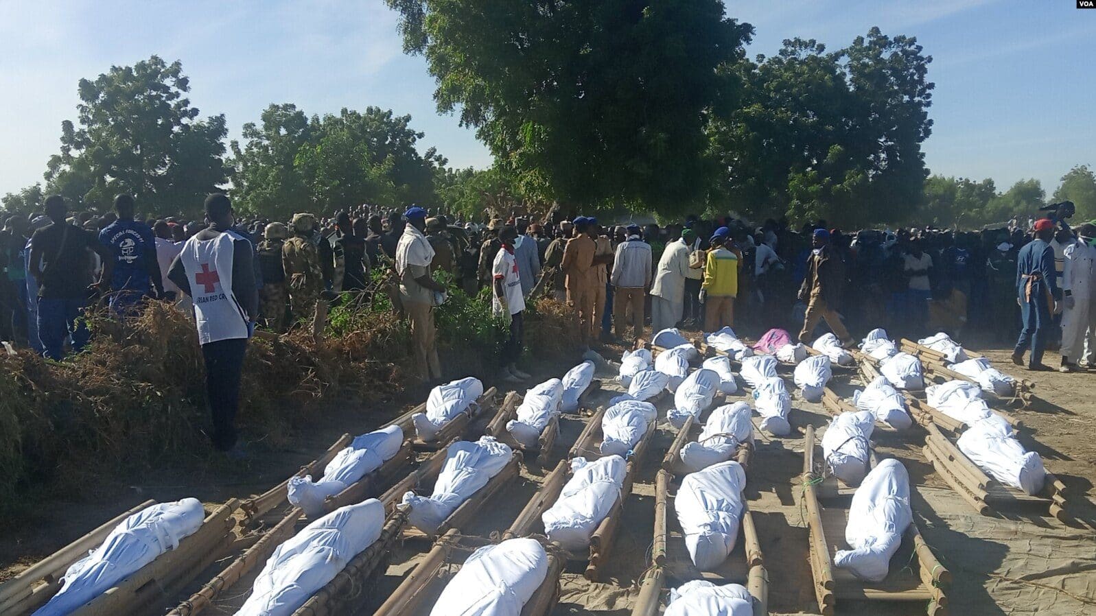 Mourners and Red Cross volunteers gather beside rows of shrouded bodies at the funeral for victims of the Zabarmari/Koshebe massacre, Borno State, November 2020