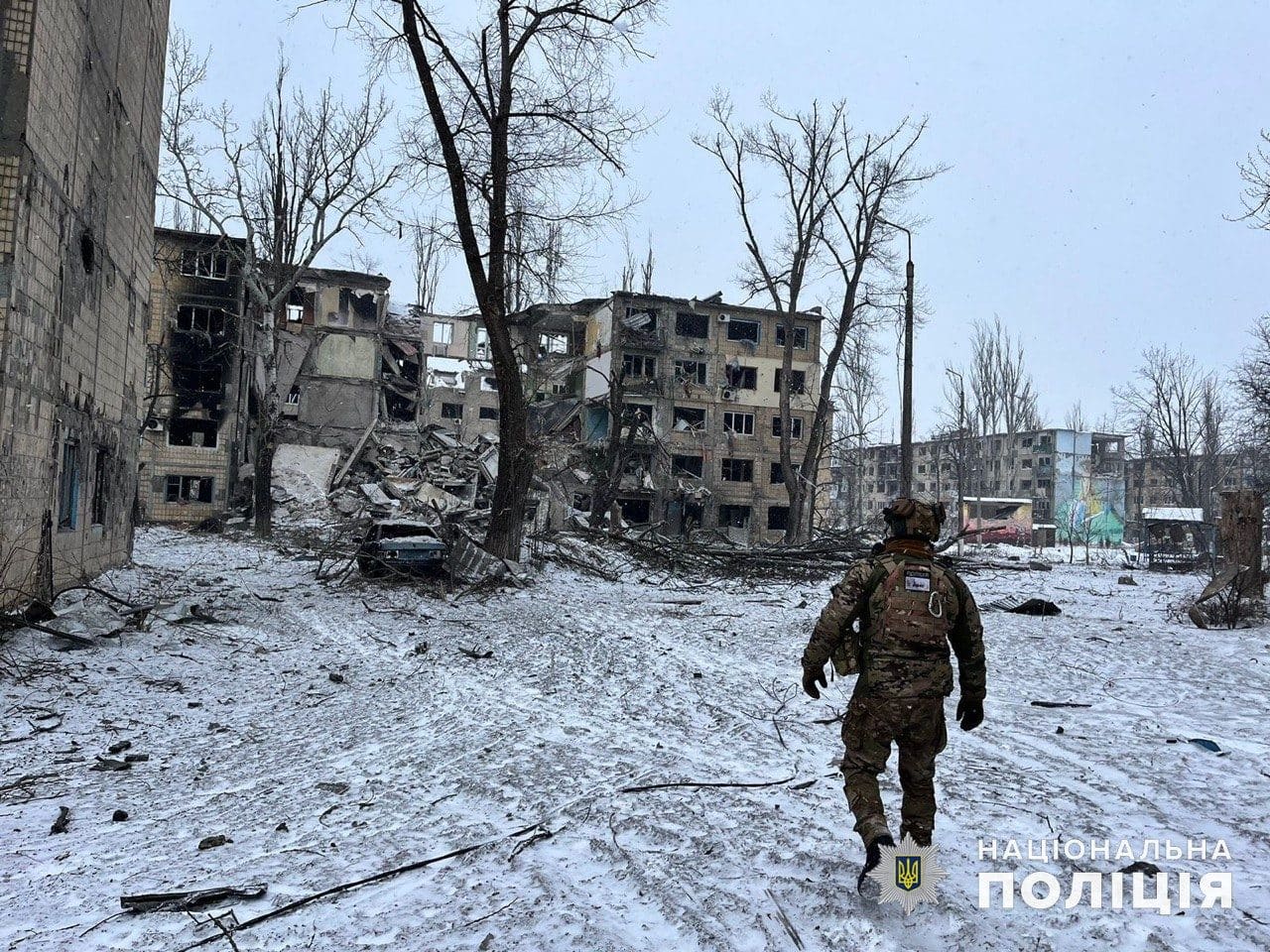 A Ukrainian police officer walking through snow past a residential building shattered by Russian bombing in Avdiivka, January 2024