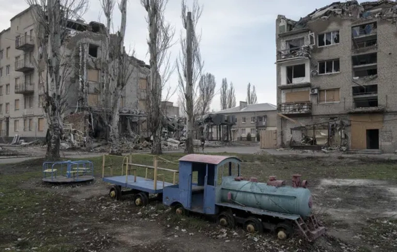 A gutted apartment block and a children's playground train in a Pokrovsk courtyard, photographed during the siege in January 2025