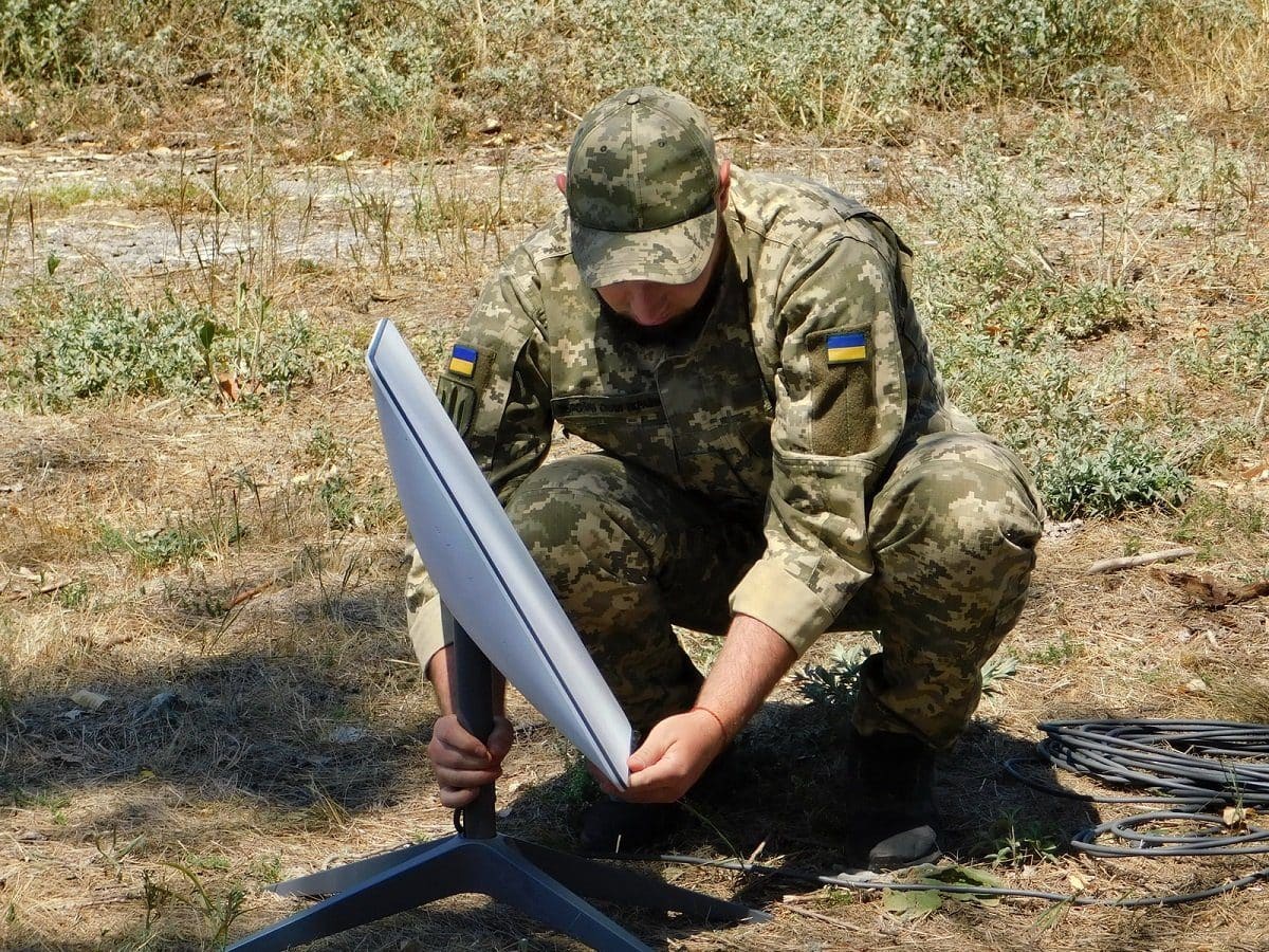 A Ukrainian soldier installing a Starlink satellite internet terminal on its tripod mount in a field