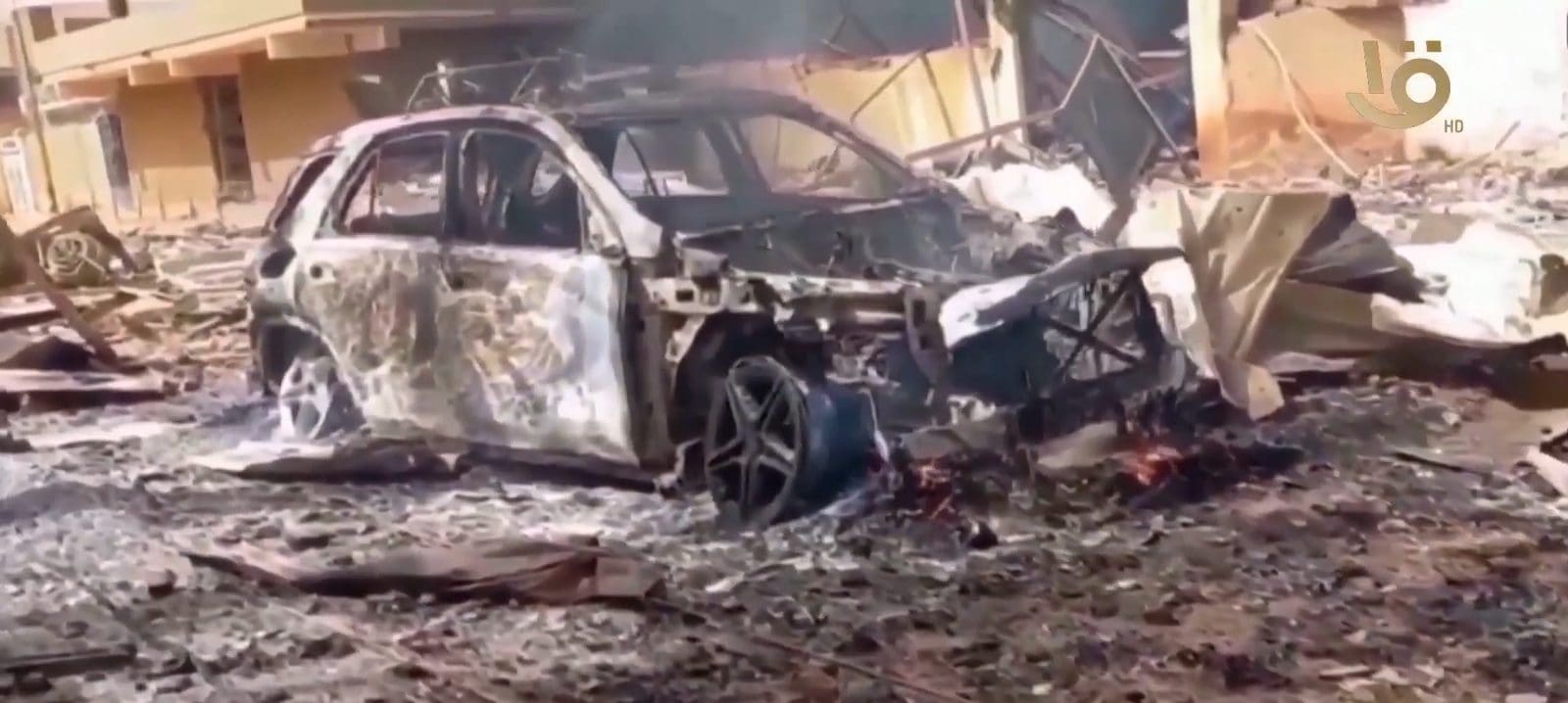 A burned-out, destroyed car sitting in a damaged street in El Fasher, North Darfur, Sudan