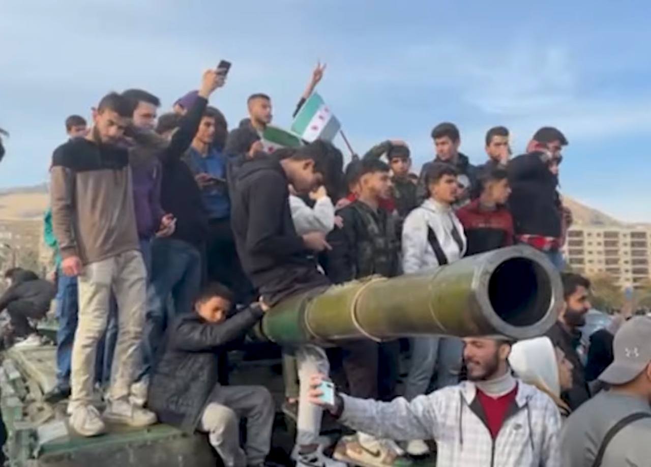 Syrian citizens celebrating on an abandoned government tank in Damascus after the fall of the Assad regime
