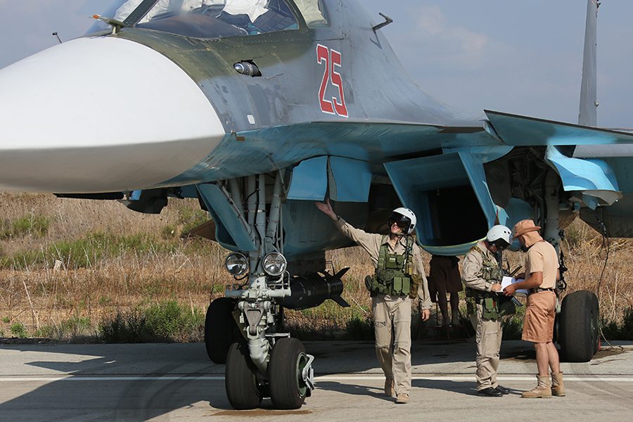 Russian ground crew performing maintenance checks on a Sukhoi Su-34 fighter-bomber on an airfield apron